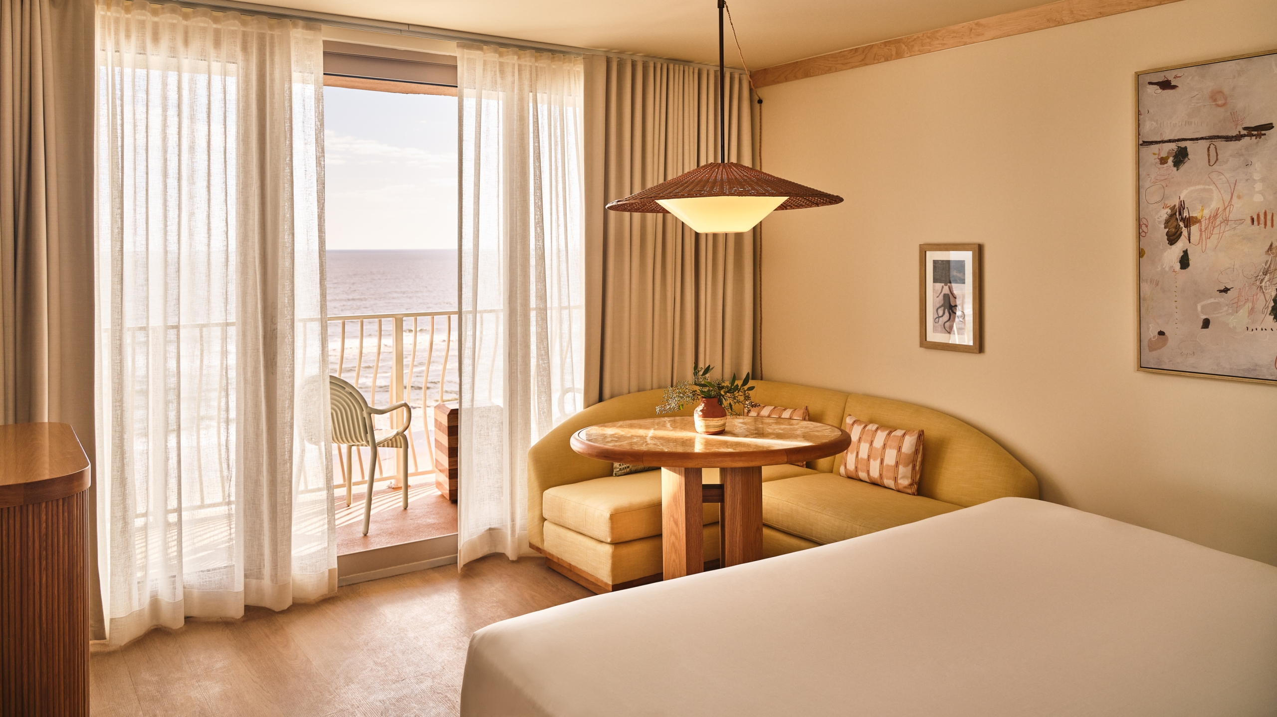A sunlit guest room featuring a mid-century modern seating nook and sheer curtains opening to the Atlantic Ocean.