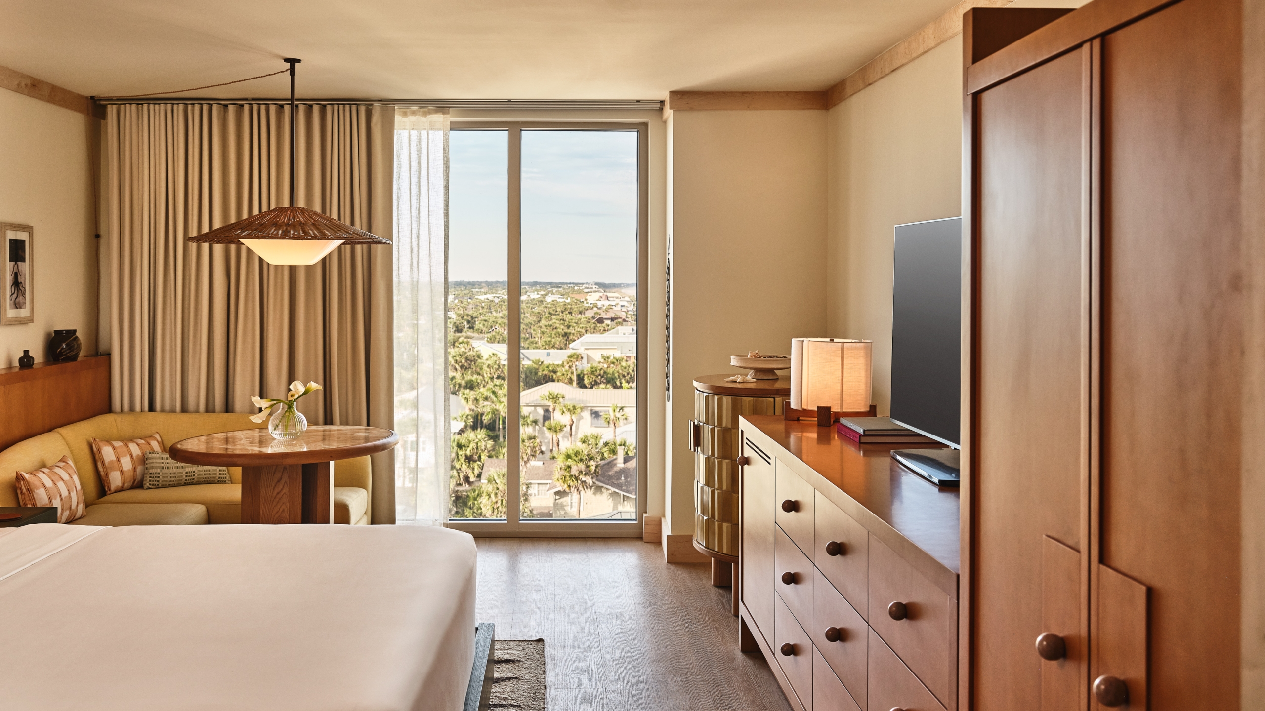 A modern hotel room interior with a large window looking out over a lush, green coastal town landscape.