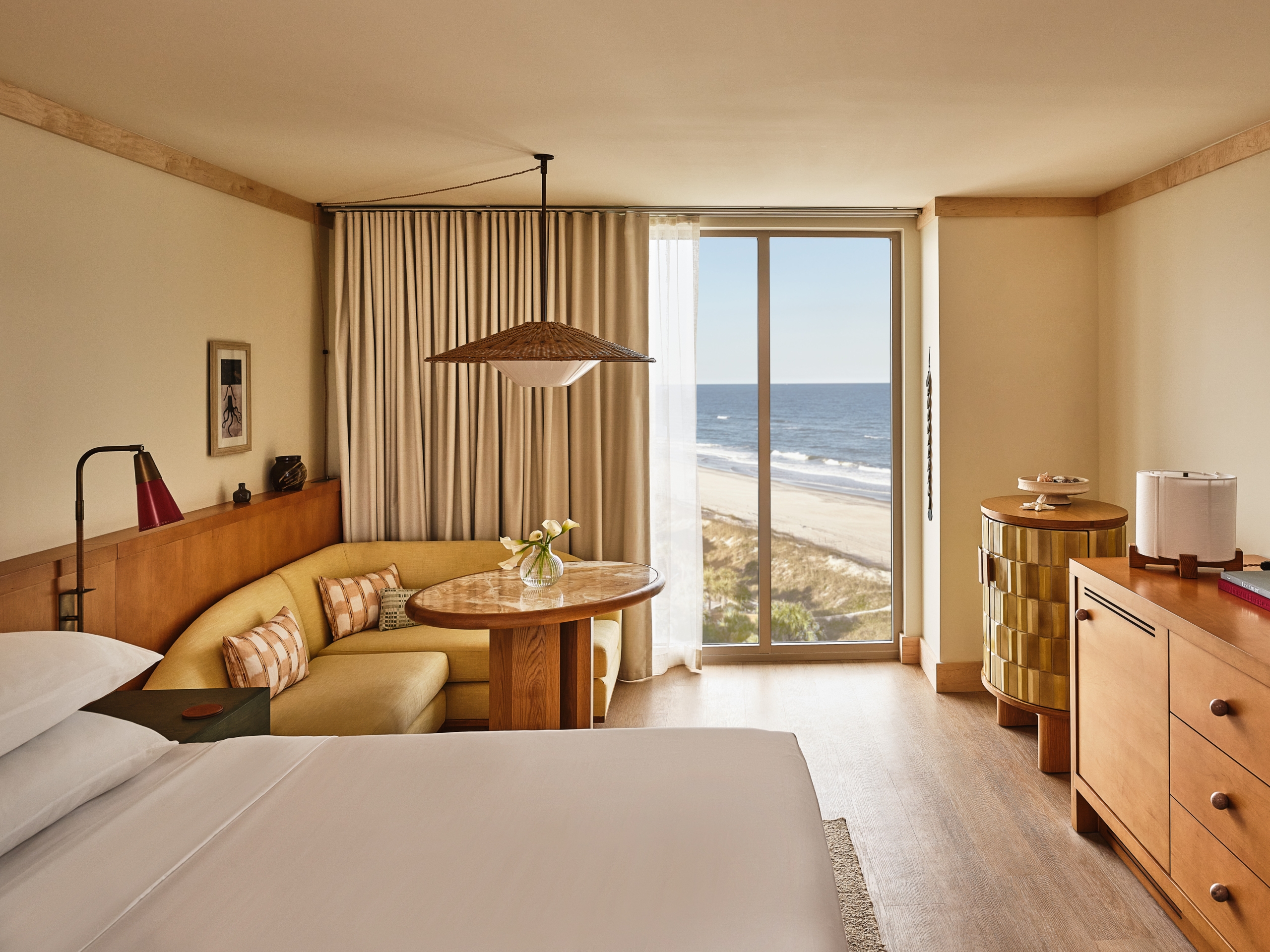 A luxury guest room with warm wood tones and a large window perfectly framing the sandy dunes and blue ocean.