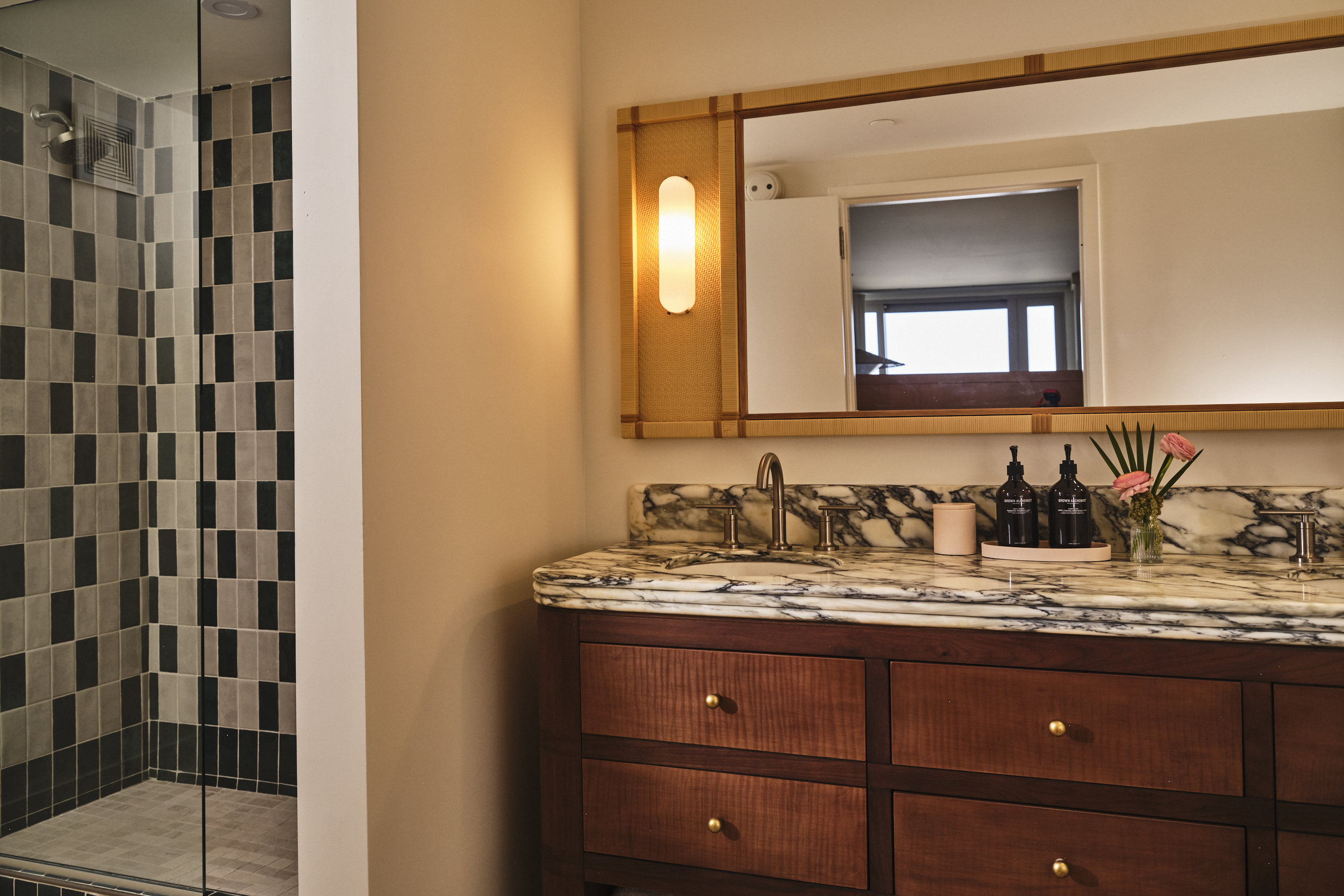 A luxury bathroom featuring a marble double vanity, a large wood cabinet, and a walk-in shower with black and white tiles.
