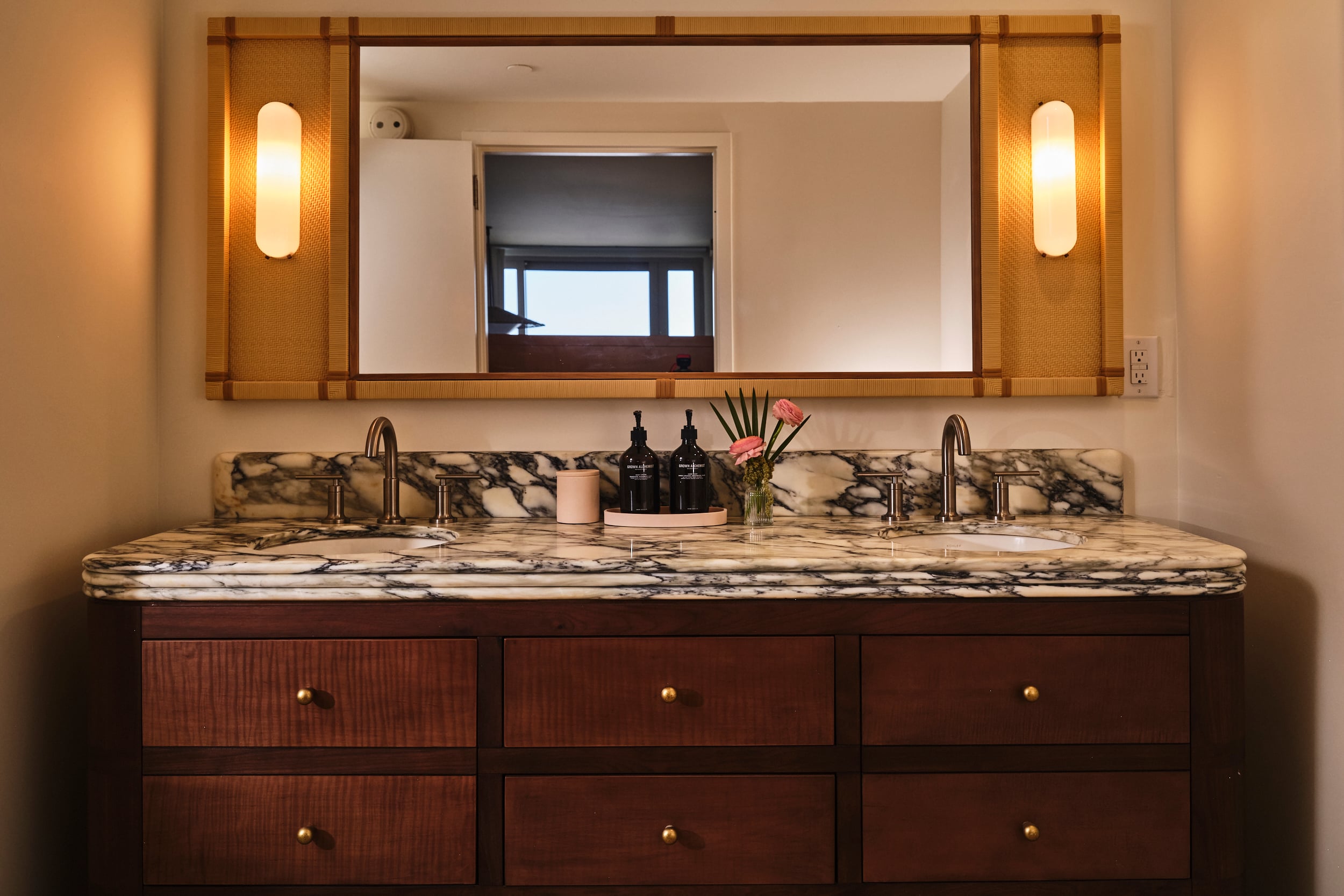 A double marble vanity with two sinks, gold fixtures, and a large wood-framed mirror with built-in sconces.
