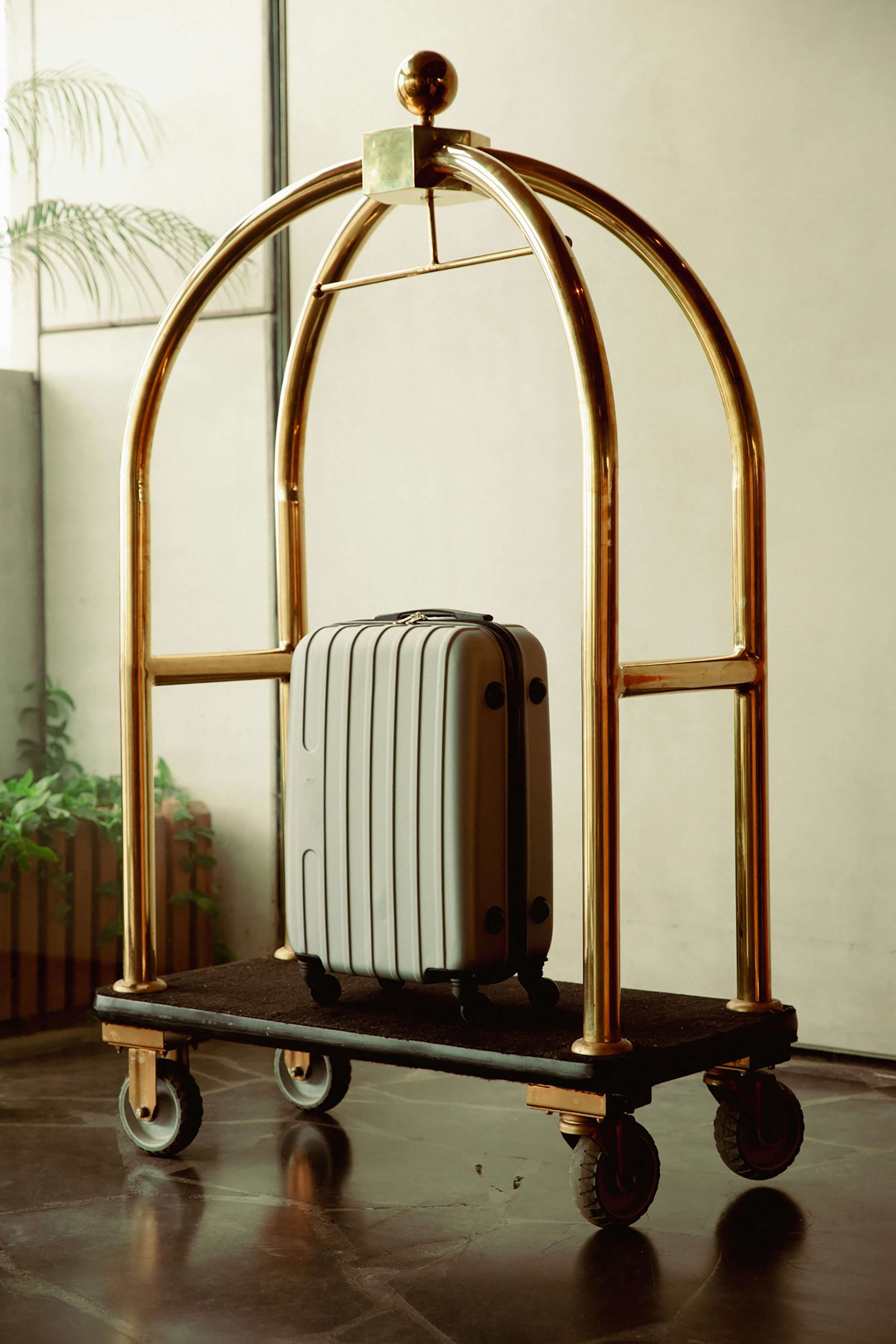 A single silver suitcase sitting on a gold-framed hotel bellman's luggage cart.