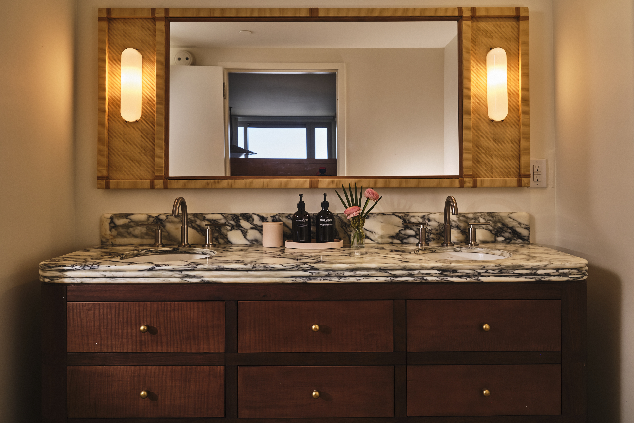 A wide marble bathroom vanity with two sinks, gold fixtures, and a large wood-framed mirror with built-in lights.